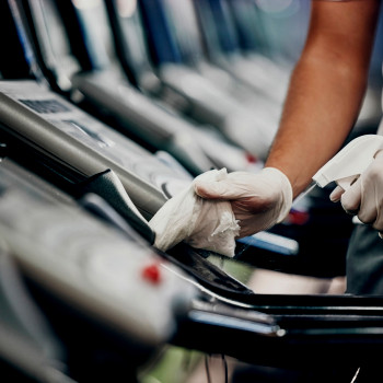 CMMS | gym maintenance worker sprays treadmills during regular cleaning schedule.