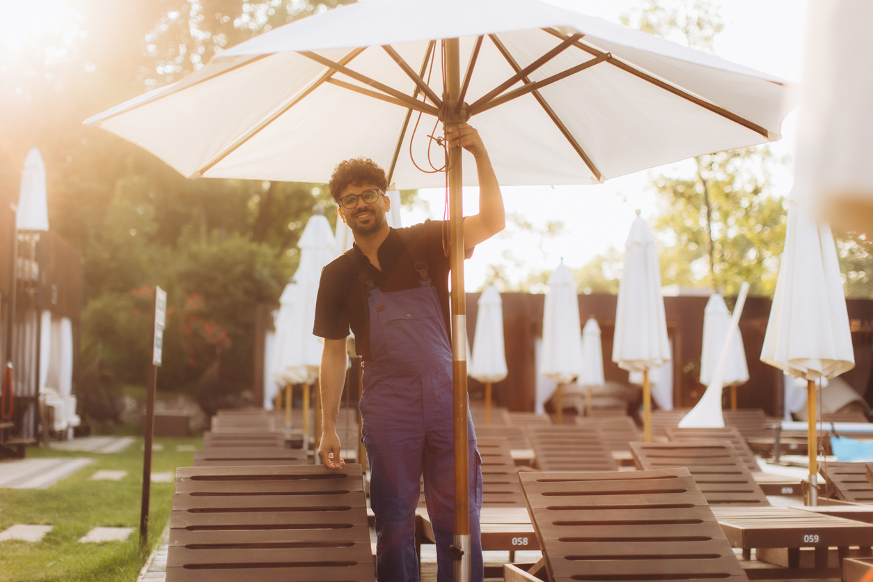 Hotel worker at poolside with chairs and umbrellas | CMMS