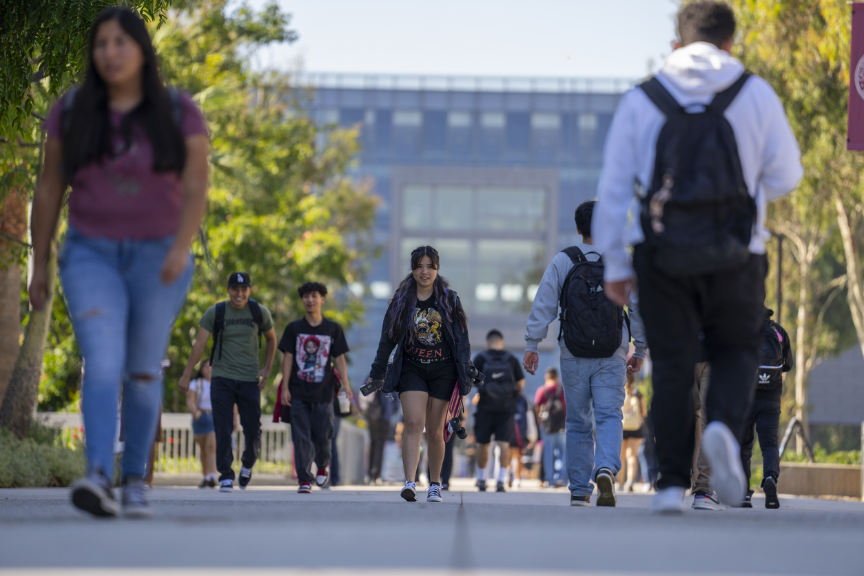 Student in focus walks along path amongst other students at a college campus