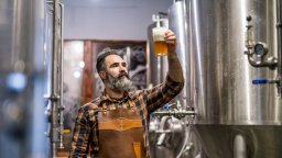 Brewer samples beer next to production equipment | Small Business