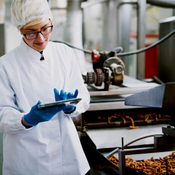 Female technician works on tablet next to food production line