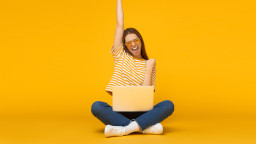 Woman sitting with laptop on legs celebrating success with yellow background