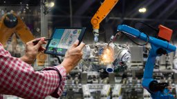Automated machine arms operate with man holding tablet with technical data in the foreground