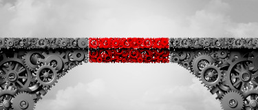 A grey bridge made of mechanical cogs including a red section of cogs added to the middle to join the two sides