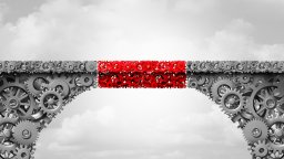 A grey bridge made of mechanical cogs including a red section of cogs added to the middle to join the two sides