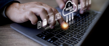 Hands typing on laptop keyboard with graphical overlay representing data backup to the cloud