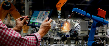Automated machine arms operate with man holding tablet with technical data in the foreground