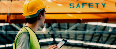 CMMS | Maintenance workers with mobile CMMS in front of safety sign