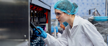 Maintenance worker in lab coat and hair net tests a machine with handheld device