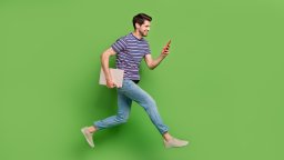 man with a laptop under the arm and a mobile phone in the hand jumps in the air with green background