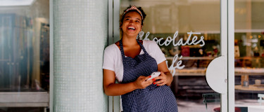Lady leans on post near entrance to a chocolate shop