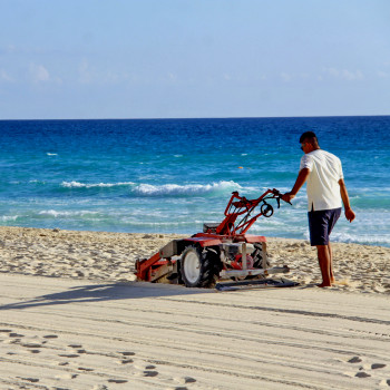 Maintenance worker smoothes sand at beachside resort | CMMS