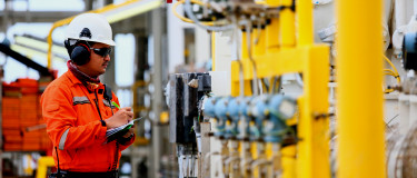 maintenance worker at a gas wearing orange overalls and hardhat plant performs preventive maintenance checks.