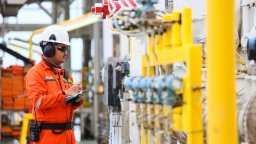 maintenance worker at a gas wearing orange overalls and hardhat plant performs preventive maintenance checks.