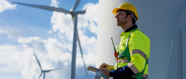 CMMS | Wind maintenance technician holding tablet looks toward wind turbines
