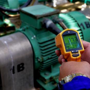 Maintenance worker hands hold temperature gauge to check motor temp metric.
