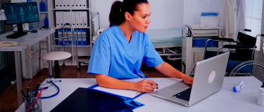 Doctor sits at desk looking at computer | CMMS