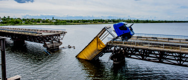 Section of a bridge over water has given way to a truck that has fallen into the river